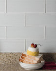 Textured White Glass Subway Tile Kitchen Backsplash Behind Speckled Countertop with Vases and Plates of Food