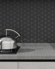 Gray Kitchen Countertop and Tea Kettle on Burner in Front of Matte Black Ceramic Triangle Mosaic Tile Backsplash