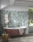 Rustic bathroom featuring a bronze red clawfoot tub and tiled tub surround made out of glossy blue-gray ceramic 4x4 square tiles.